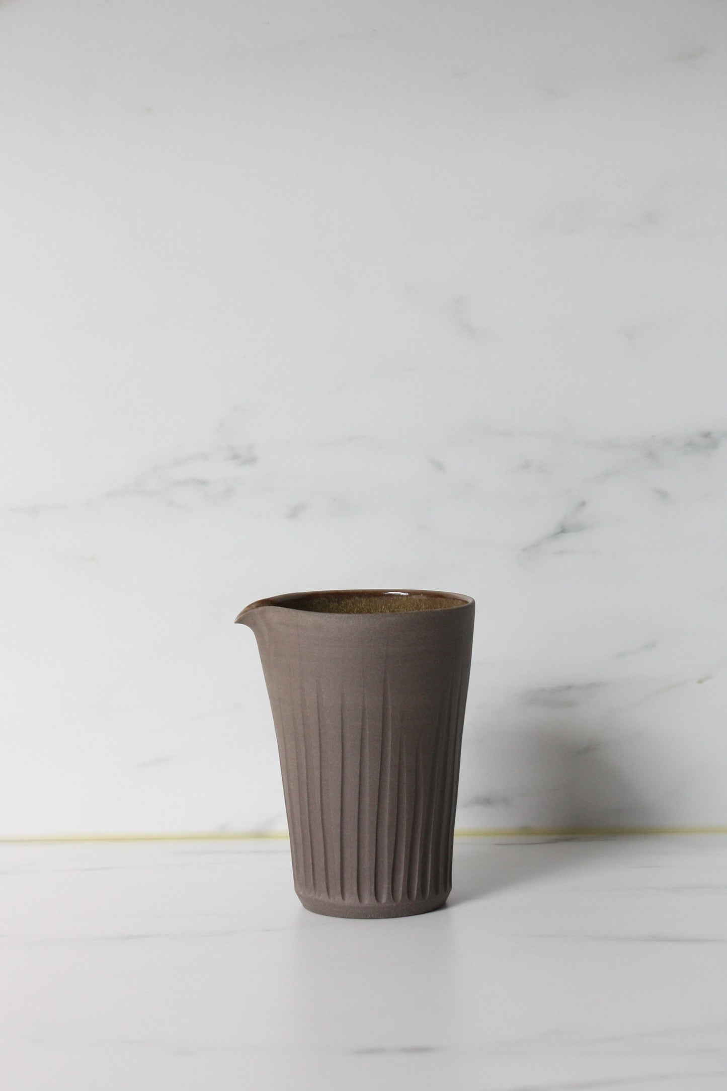 Photo of a grey coloured clay milk pourer on a white marble background.