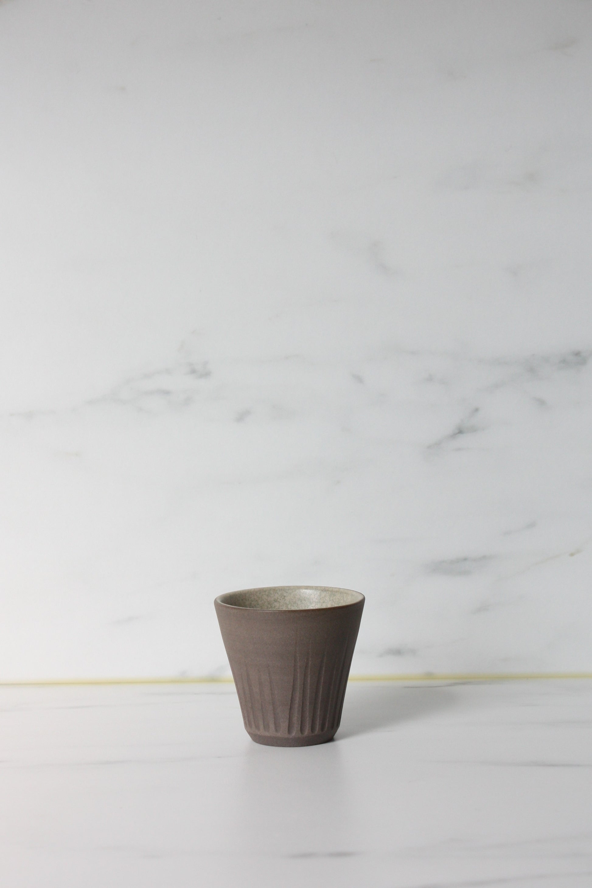 Photo of a grey coloured clay espresso pot on a white marble background.
