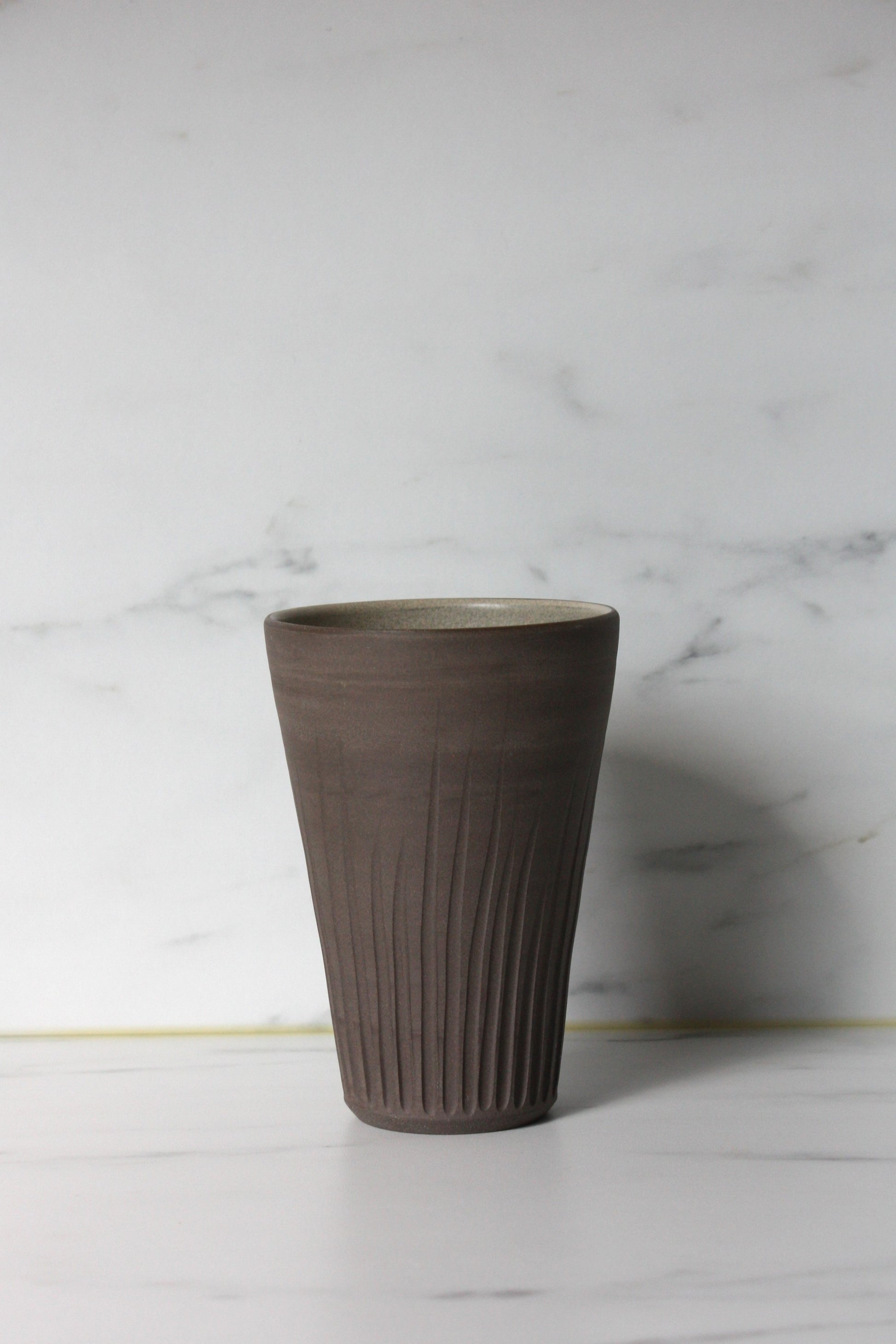 Photo of a large charcoal coloured clay beaker on a white marble background.