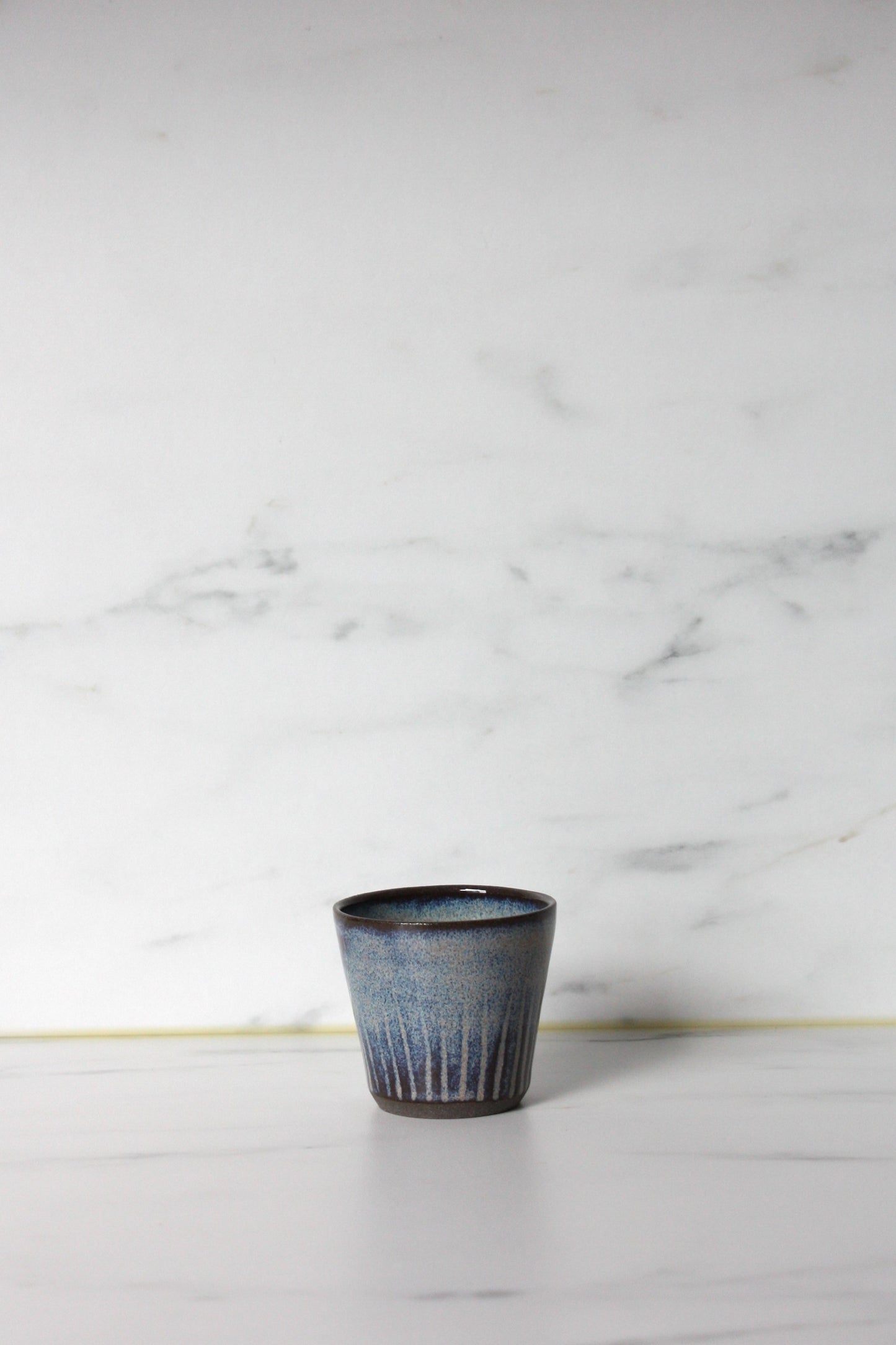 Blue glazed straight sided espresso pot on a white marble background.