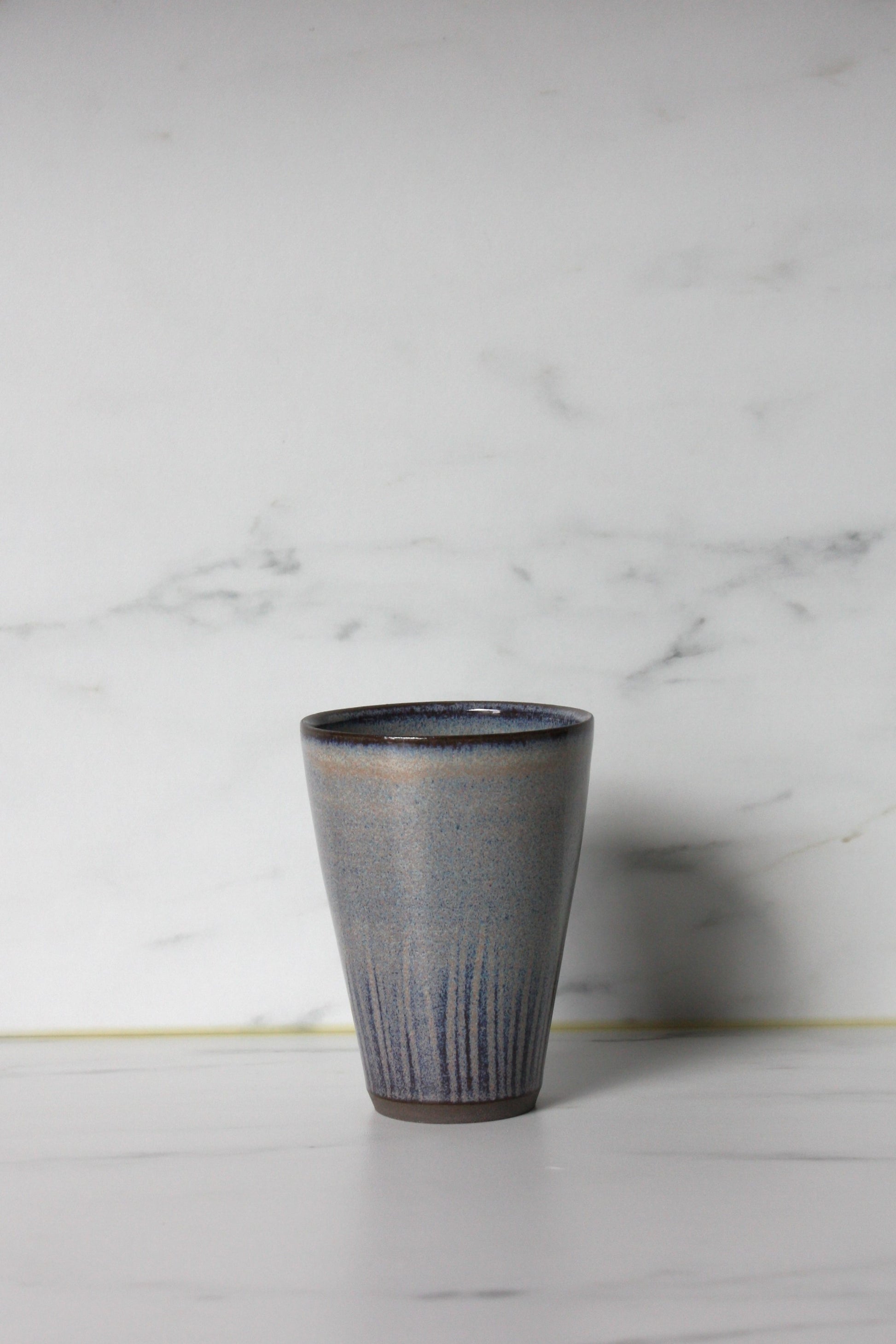 Blue glazed straight sided beaker on a marble background.