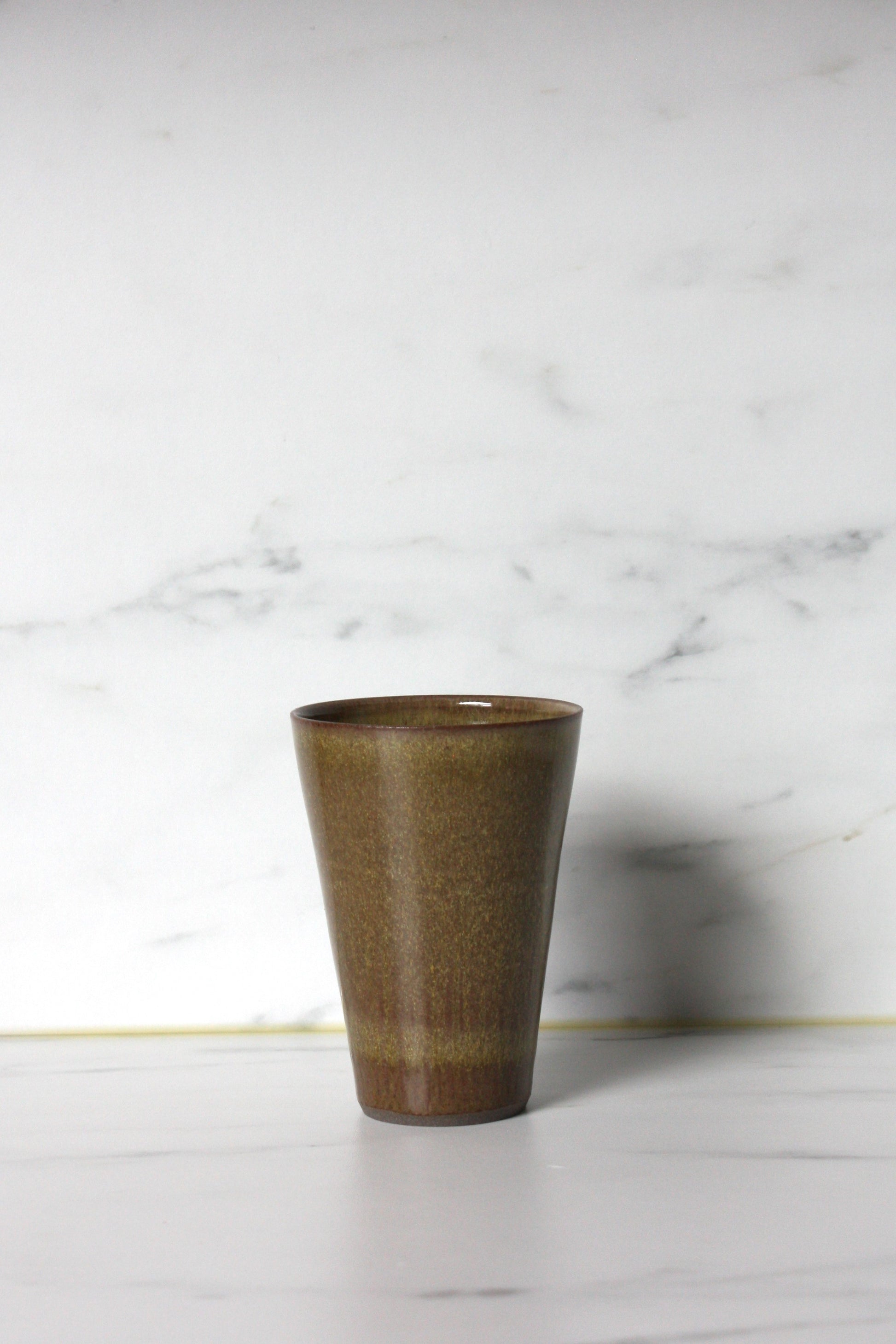 Photo of a moss coloured straight sided beaker with a marble background.