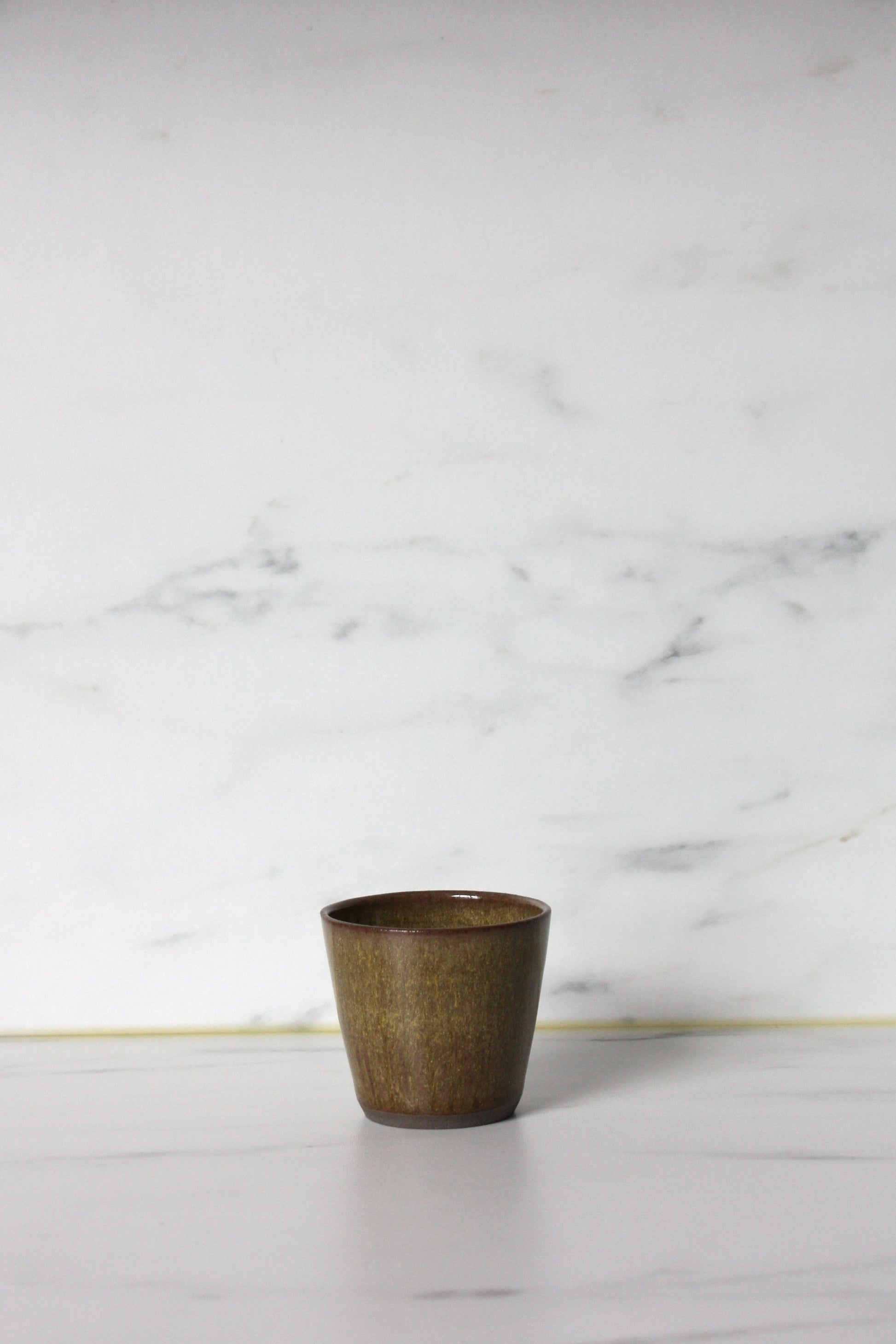 Photo of a moss coloured straight sided espresso pot with a marble background.